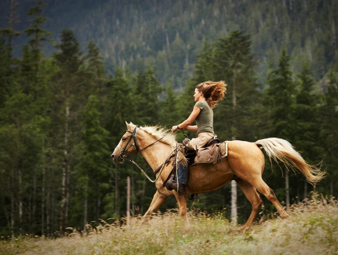 A woman rides a horse through a forest landscape.