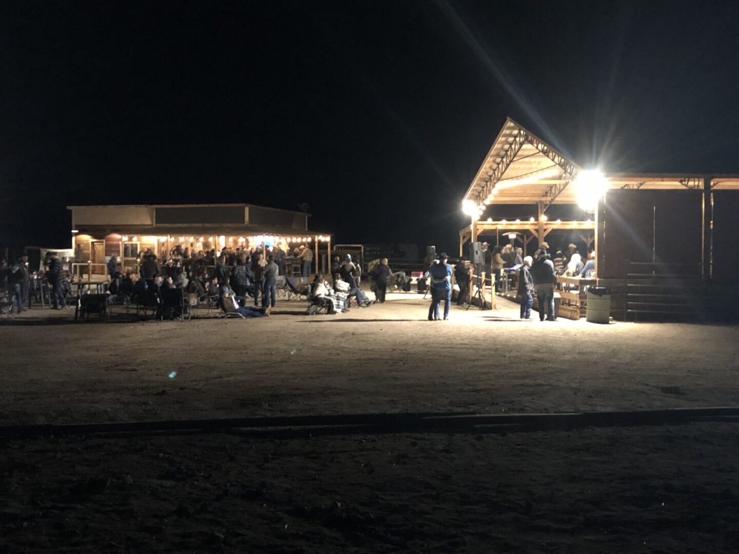 A nighttime gathering with people near a brightly lit wooden pavilion.