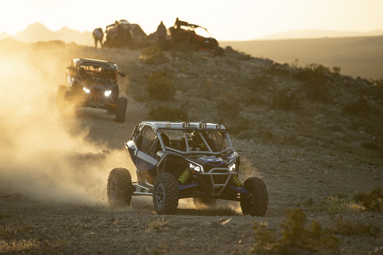 Off-road vehicles racing on a dusty desert trail at sunset.
