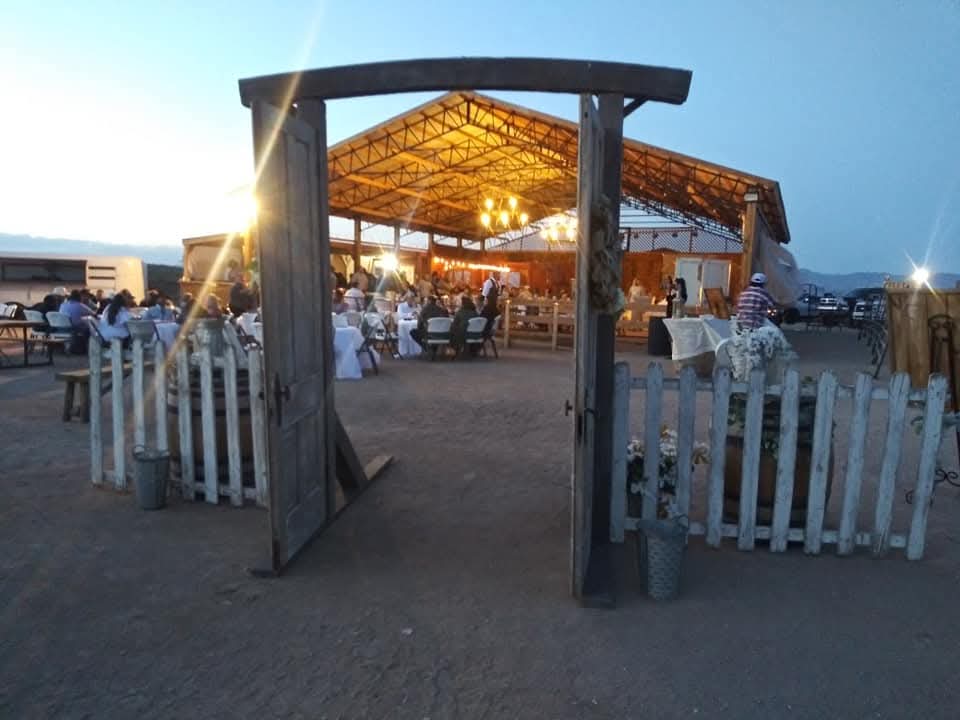 Open wooden gate leading to a lit outdoor event at dusk.