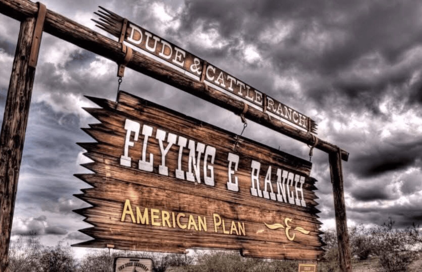 Rustic wooden sign for Flying P Ranch under a dramatic cloudy sky.